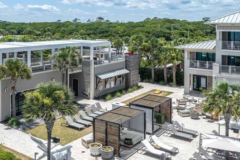 Aerial view of multi-level resort with rooftop lounge, palm trees, modern architecture, and natural preserve