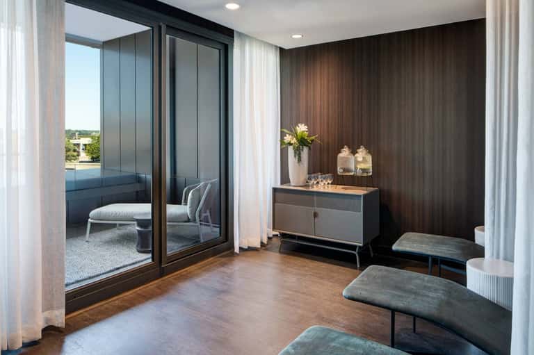 Luxury suite interior with glass doors opening to balcony, dark wood accent wall, and modern furnishings