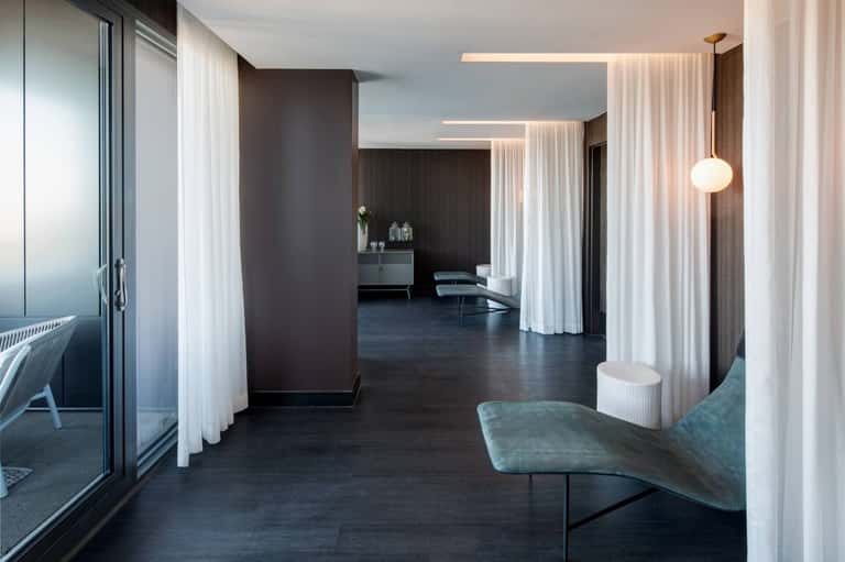 Minimalist spa corridor with white flowing curtains, dark flooring, and contemporary pendant lighting