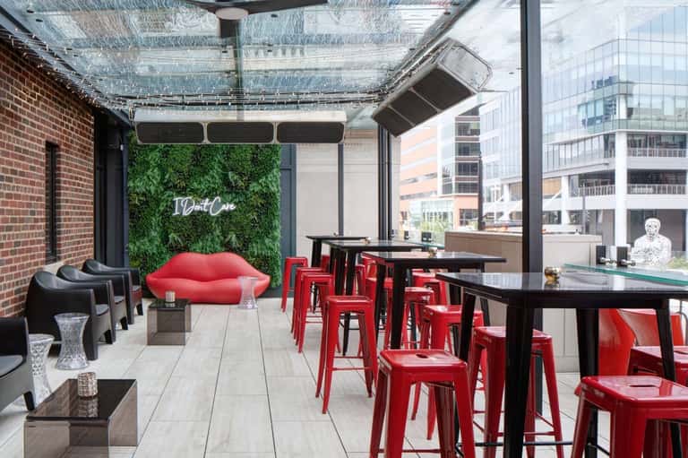 Urban rooftop bar with red chairs, green living wall, and city skyline views