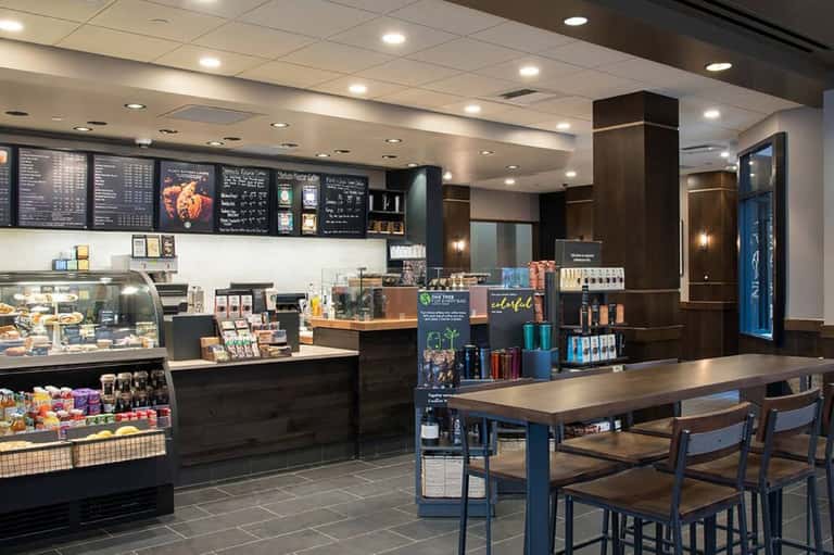Modern hotel cafe interior with dark wood counters, menu boards, pastry display, and seating area