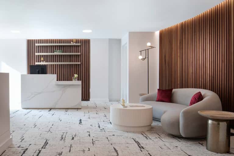 Modern hotel lobby with curved furniture, wooden slat wall paneling, marble flooring, and reception desk