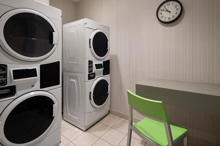 Hotel laundry facility with stacked washers and dryers, folding table, and wall clock