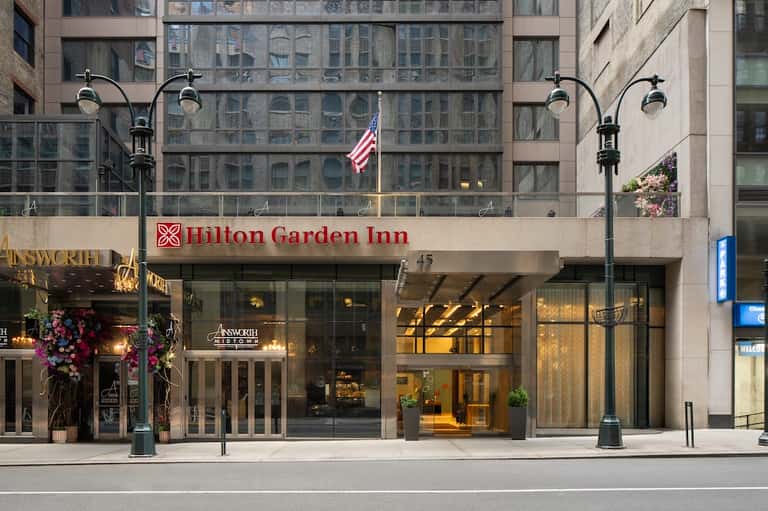 Hilton Garden Inn storefront on urban street with large windows, signage, and American flag display