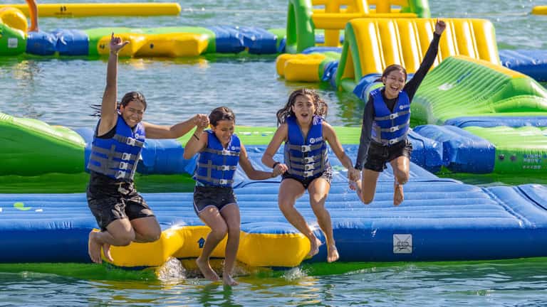 Children in life vests playing on colorful inflatable water park obstacles in ocean