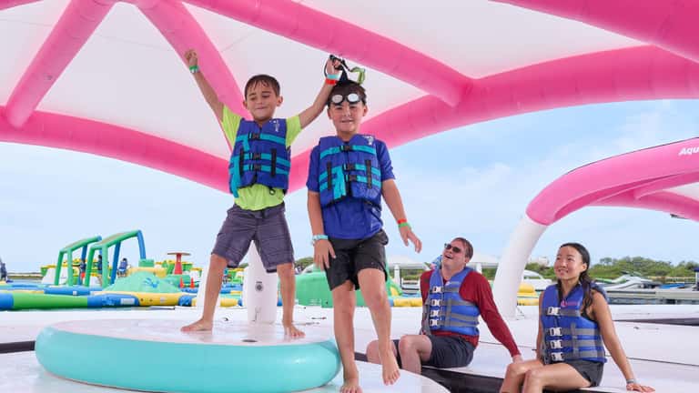 Children in life jackets playing on inflatable water obstacle course structure