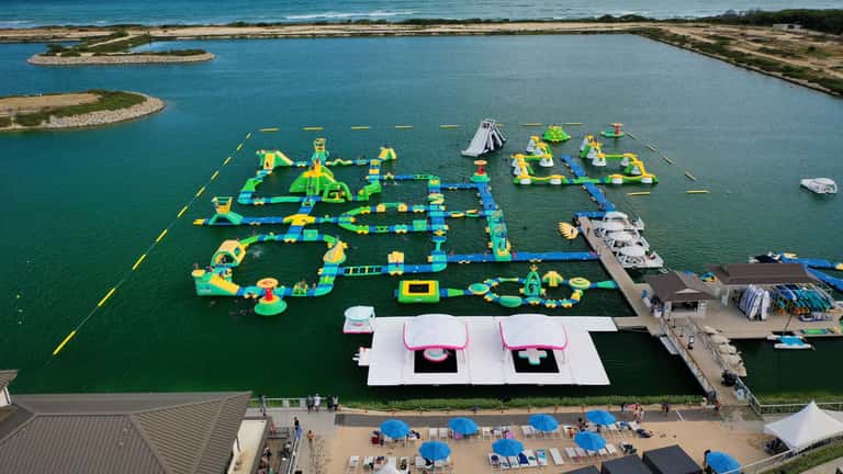 Aerial view of large inflatable water park with colorful yellow and blue obstacles in turquoise lagoon