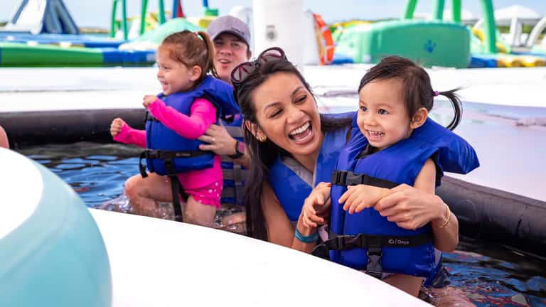 Woman with two young children in life jackets enjoying water activities at resort pool