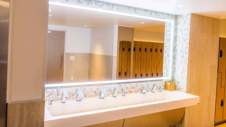 Contemporary bathroom with long white vanity counter, illuminated mirror, and wooden lockers