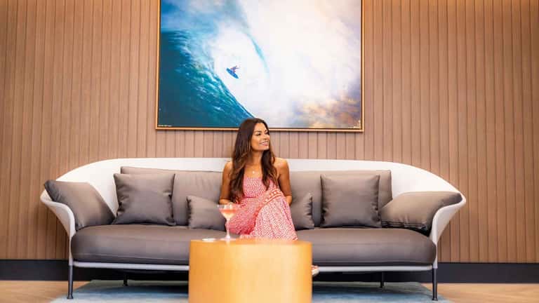 Woman on modern sofa in elegant lobby with surfing artwork and wood paneling