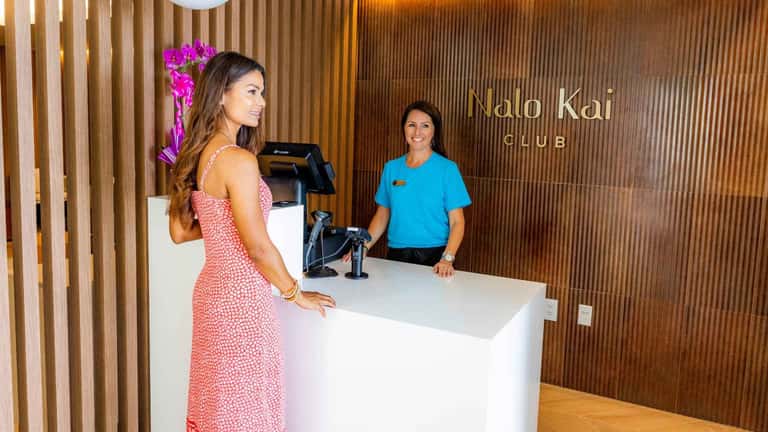 Nalo Kai Club reception desk with staff member greeting guest in warm wooden-paneled interior