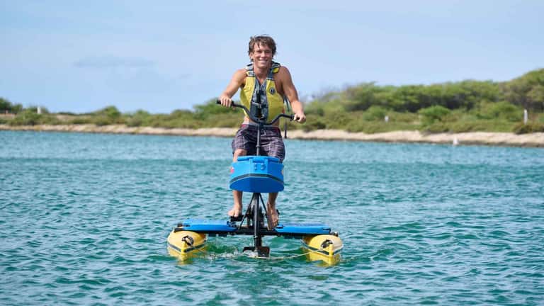 Man riding water bike with outriggers across turquoise ocean water near coastal landscape