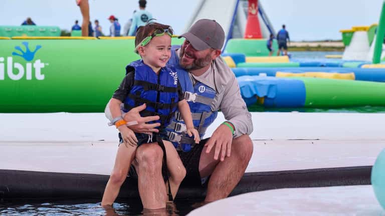 Father and child in life jackets at water sports obstacle course with inflatable equipment and lake backdrop