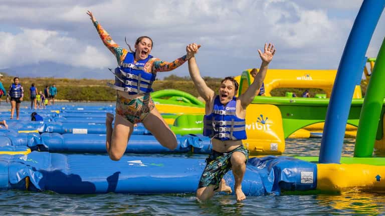 Two people jumping on blue and yellow inflatable water park obstacle course in lake