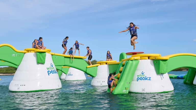 Inflatable water playground obstacle course with children jumping and climbing in turquoise water