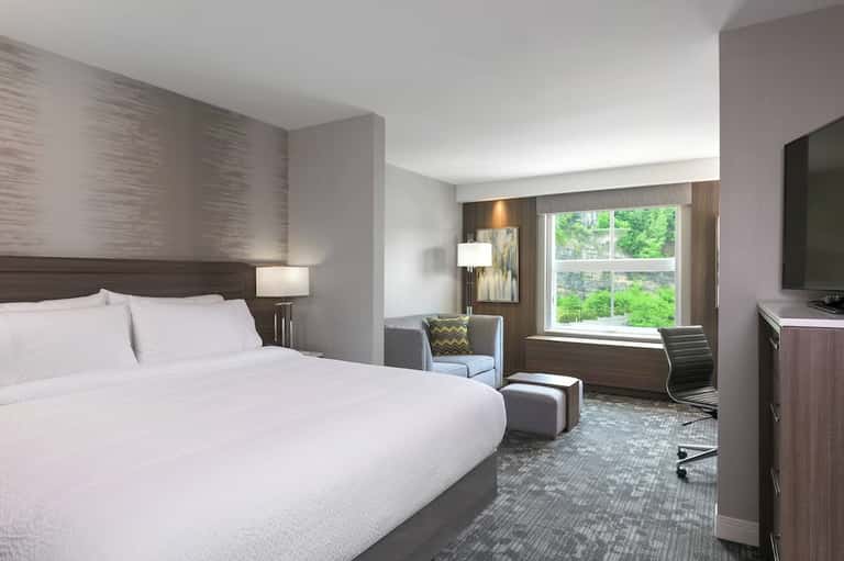 Contemporary hotel bedroom with queen bed, workspace, and scenic window view