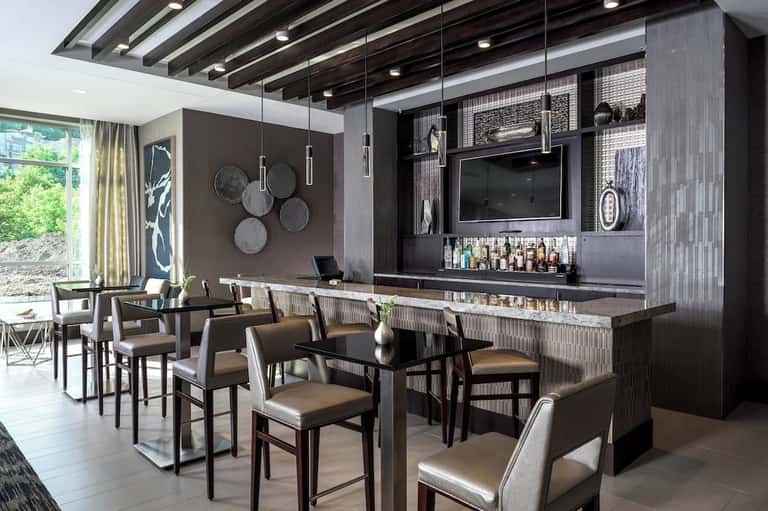 Contemporary hotel bar with dark wood cabinetry, pendant lighting, flat-screen TV, and bar seating