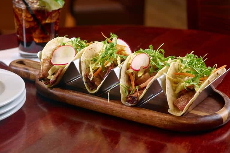 Gourmet tacos with radish, greens, and protein on wooden serving board