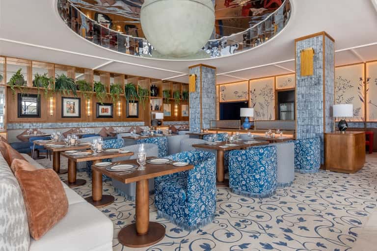 Modern upscale restaurant with blue patterned chairs, wooden tables, and architectural ceiling detail