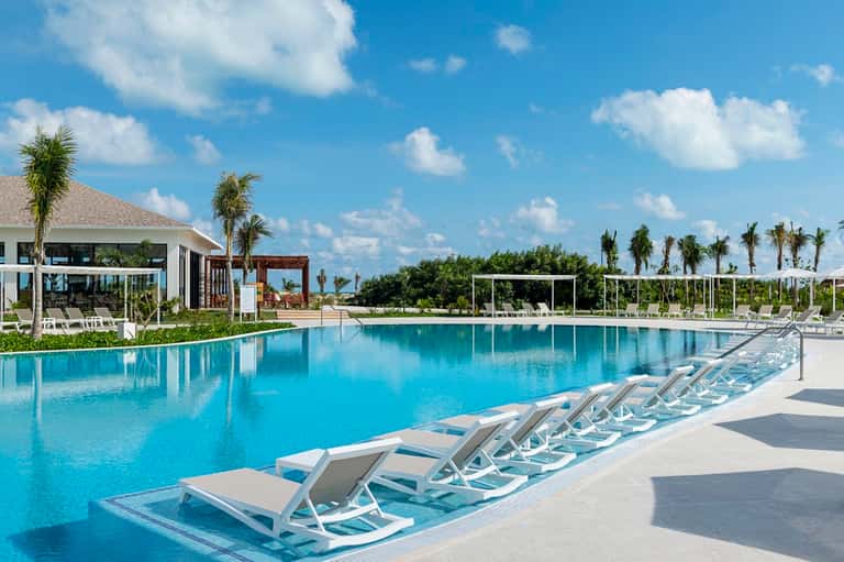 Rectangular resort pool with white loungers, cabanas, and manicured landscape