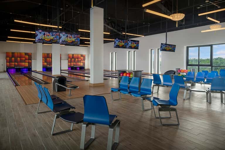 Bowling alley with multiple lanes, blue seating, and windows overlooking resort landscape