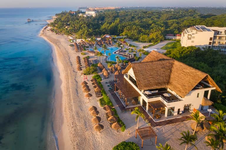 Aerial view of beachfront resort with thatched-roof structures, pools, and pristine white sand beach