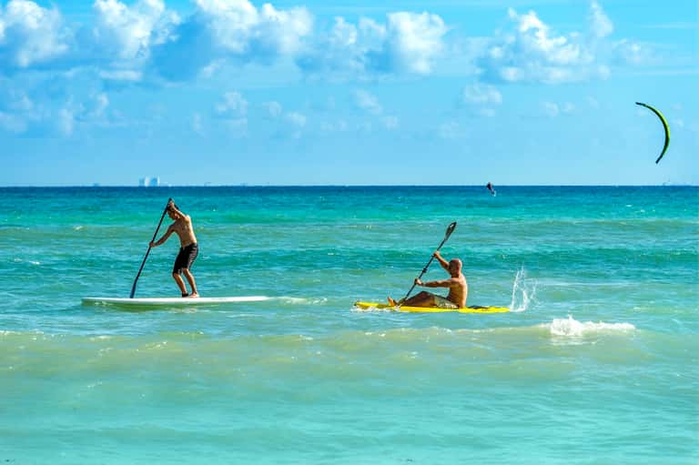 Beachgoers paddle boarding and kiteboarding in turquoise tropical ocean waters