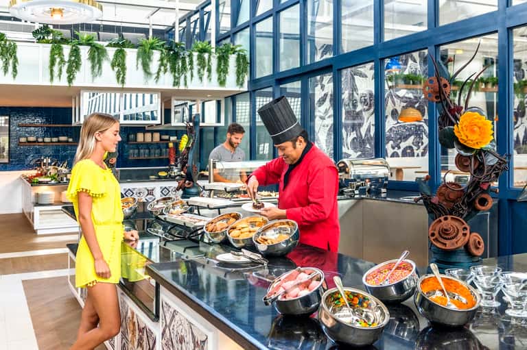 Chef in red jacket preparing food while woman in yellow watches in modern kitchen