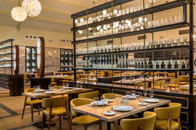 Upscale restaurant interior with yellow chairs, black shelving, and wine display