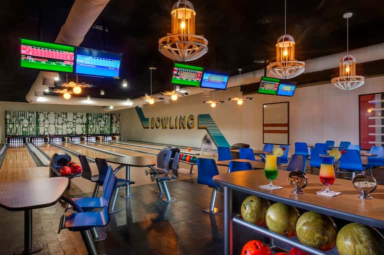 Bowling alley with lanes, colorful chairs, cocktails, and illuminated pendant lights