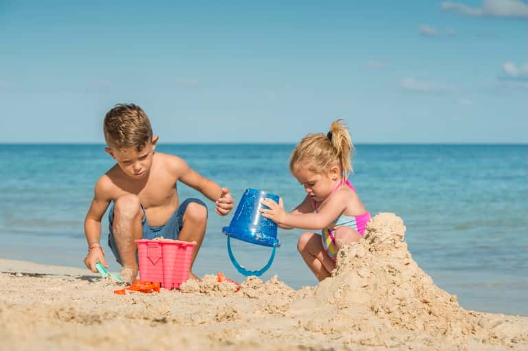 Children building sandcastle on beach with ocean and blue sky in background