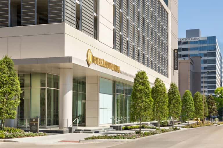 Modern hotel exterior entrance with gold signage, glass doors, and manicured landscaping