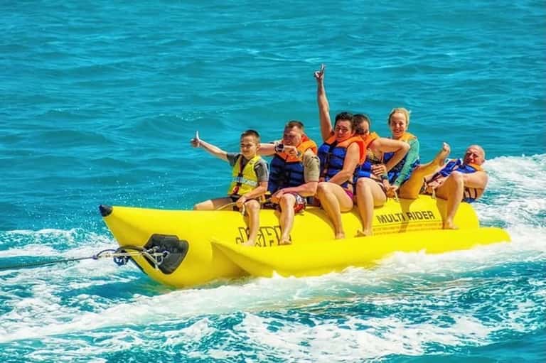 Family of six on bright yellow banana boat enjoying water sports in turquoise ocean
