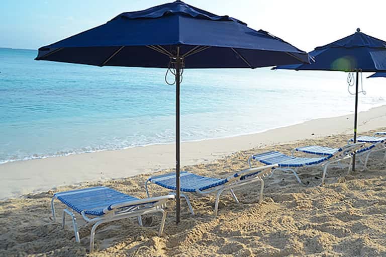 Blue umbrellas and lounge chairs on sandy beach with clear turquoise ocean water