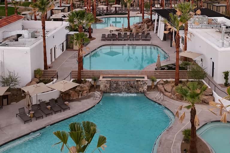 Aerial view of resort pool complex with multiple pools, palm trees, loungers, and buildings