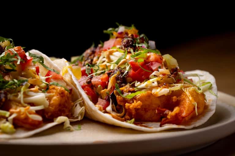 Gourmet fried shrimp tacos with fresh toppings and colorful garnish on white plate