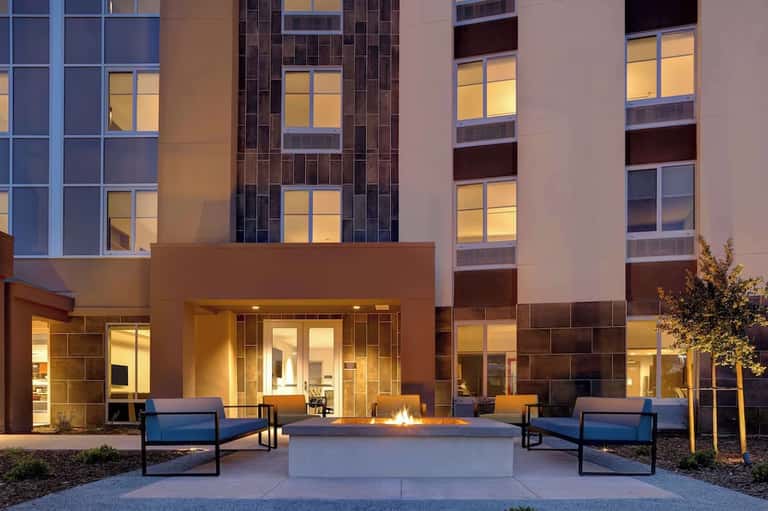 Modern hotel courtyard with firepit, blue lounge chairs, and illuminated building facade
