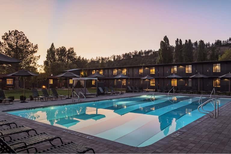 Lap pool at dusk with illuminated cabins and forested mountains in background