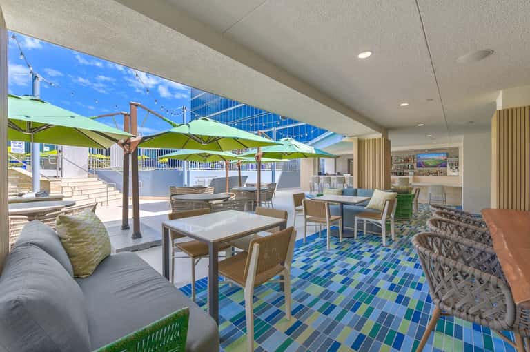 Modern lounge area with lime green umbrellas, white furniture, blue mosaic tile floor, and indoor-outdoor design