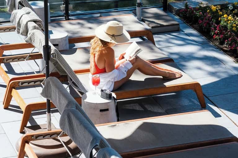 Woman lounging on padded deck chair with cocktail, ocean views, and flowering garden backdrop