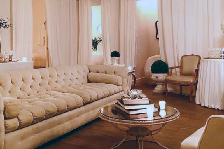 Luxury spa lounge with quilted beige sofa, cream armchairs, floor-to-ceiling windows, and warm lighting