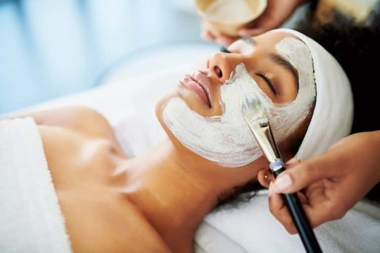 Client receiving facial mask application with brush by spa professional during treatment
