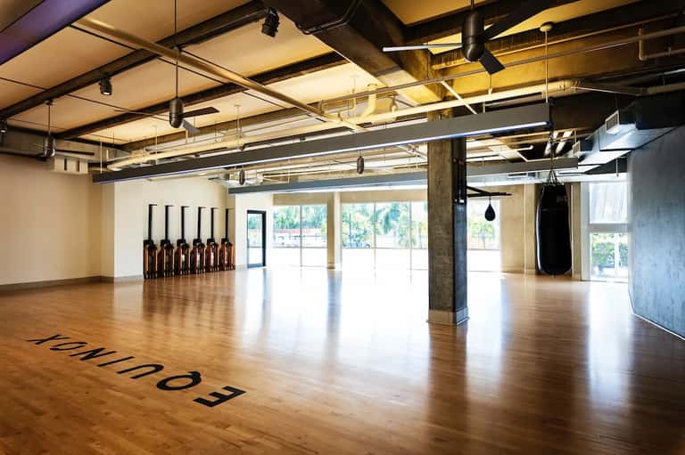 Spacious boxing and fitness studio with wooden flooring, punching bags, and natural lighting