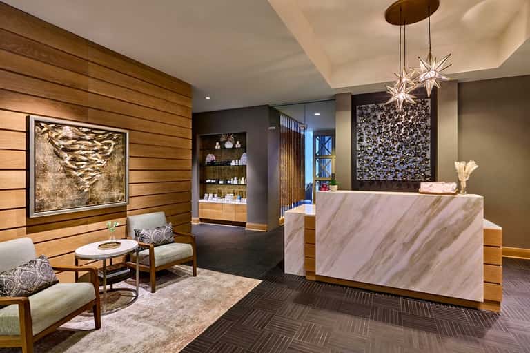 Modern hotel reception area with marble counter, wood paneling, and contemporary chandelier