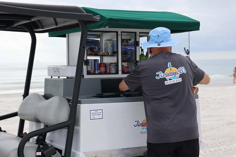 Beach bar attendant at Jimmp's Beach Bar kiosk with green canopy on sandy beach near ocean