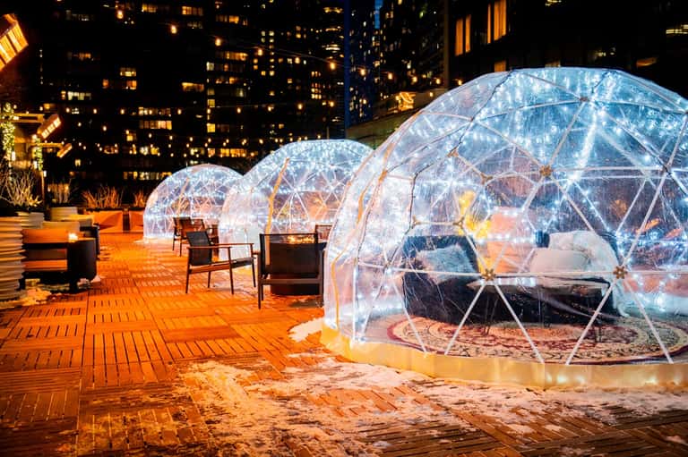 Illuminated dining domes on rooftop terrace with city skyline at night