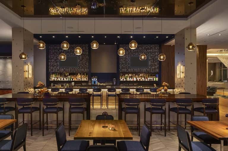 Hotel bar lounge with gold pendant lighting, dark wood accents, patterned wall panels, and modern seating