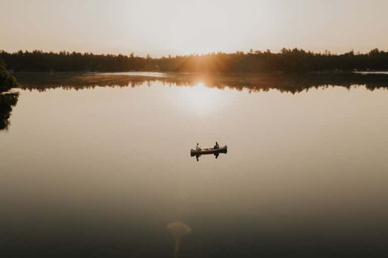 Two people in canoe on mirror-still lake at golden hour sunrise