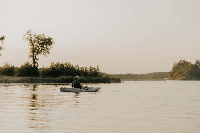 Person in kayak on calm river with forested shoreline in background
