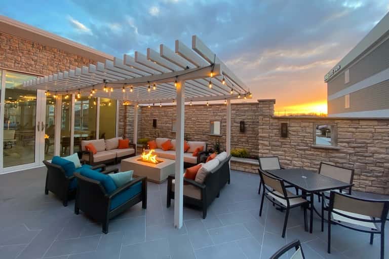 Modern patio with pergola, fire pit, colorful seating, and sunset views at dusk